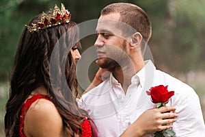 Beautiful romantic couple kiss closeup. Attractive young woman in red dress and crown with handsome man in white shirt