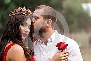 Beautiful romantic couple kiss closeup. Attractive young woman in red dress and crown with handsome man in white shirt
