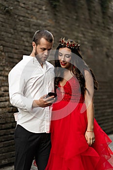 Beautiful romantic couple taking selfie. Attractive young woman in red dress and crown with handsome man in white shirt