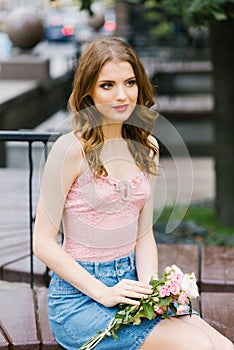 Beautiful romantic girl in a pink top and denim skirt holding a bouquet of roses