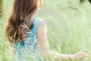 Beautiful romantic girl sitting on field of spikelets and enjoying nature, back of young elegant woman walking in long blue