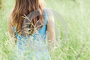Beautiful romantic girl sitting on field of spikelets and enjoying nature, back of young elegant woman walking in long blue