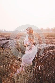 Beautiful romantic model girl outdoors dressed in tende long dress in the field in sunset light. Wind blowing long hair. Glow Sun