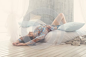 Beautiful romantic woman / girl brunette lying on the bed in her room at home. Dressed casual shirt, Sun Light, toned warm colors