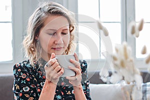 Beautiful romantic young blonde woman in dress with cup of tea sitting by the window. Feminine jewelry, mehendi