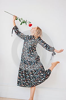 Beautiful romantic young blonde woman in dress with red rose on white walll background, full length portrait