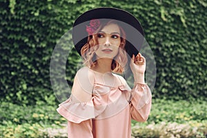 Beautiful romantic young woman on a background of natural  green wall of plants posing with flowers in head hair. Summer vibes.