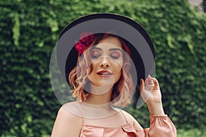 Beautiful romantic young woman on a background of natural  green wall of plants posing with flowers in head hair. Summer vibes.