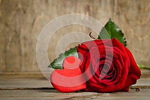 Beautiful rose and one handmade heart on the wooden board