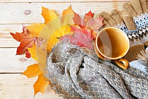 Autumn fall leaves, hot steaming cup of morning coffee and a warm scarf on wooden background,