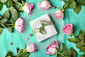 Beautiful roses and gift box on color background