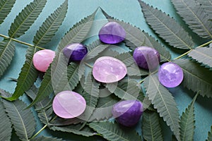 Beautiful round amethyst stones and rose quartz with a green branch on a green background. Healing crystals