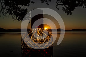 Beautiful rum bottle full with rum holding in front of a sunset over Watson Taylors Lake at Crowdy Bay National Park