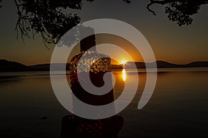 beautiful rum bottle full with rum holding in front of a sunset over Watson Taylors Lake at Crowdy Bay National Park, New South