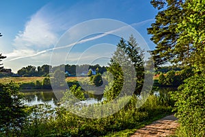 Beautiful rural landscape. Residential house near the river. Trees with bright greenery and blue sky with beautiful clouds. Summer