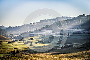 Beautiful rural mountain landscape in the morning light with fog, old houses and haystacks