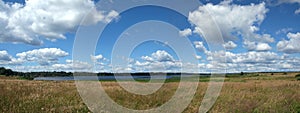 Beautiful rural panoramic landscape with lake after meadow and white clouds on blue sky on sunny summer day