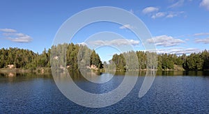 Beautiful rural summer landscape with still lake and birch forest after it against blue sky with soft clouds