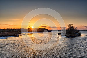 Beautiful russian early winter landscape with non frozen river, snow-covered riverside and small island at sunset. Scenic nature