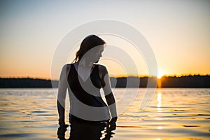 Beautiful Russian girl in a long black swimsuit swims outside the city on the lake in the rays of sunset or dawn