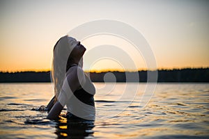 Beautiful Russian girl in a long black swimsuit swims outside the city on the lake in the rays of sunset or dawn