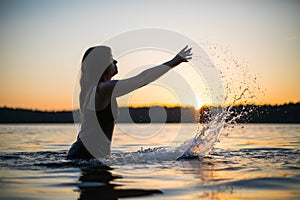 Beautiful Russian girl in a long black swimsuit swims outside the city on the lake in the rays of sunset or dawn