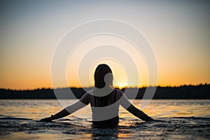 Beautiful Russian girl in a long black swimsuit swims outside the city on the lake in the rays of sunset or dawn