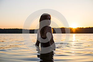 Beautiful Russian girl in a long black swimsuit swims outside the city on the lake in the rays of sunset or dawn