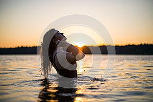 Beautiful Russian girl in a long black swimsuit swims outside the city on the lake in the rays of sunset or dawn