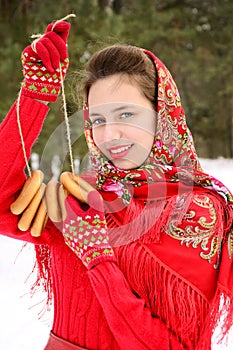 Beautiful Russian girl in a red traditional shawl holds bagels in the hands of a winter forest. Holiday seeing off winter