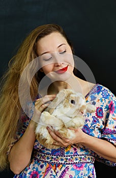 Beautiful russian woman with long blond hair holding a rabbit pet in her hands against black wall