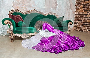 Beautiful sad crying woman in fantasy white and purple rococo style medieval dress sitting on the floor near sofa