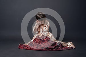 Beautiful sad crying woman in medieval style dress sitting on the floor against dark background