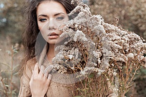 Beautiful sad cute attractive woman in a beige sweater wide in a field of dry grass in autumn cold overcast day, photo of beige