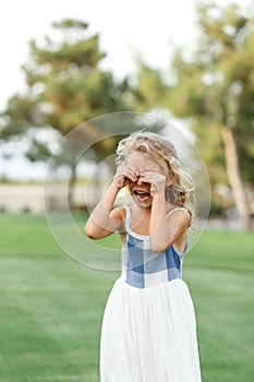 Beautiful sad little blonde curly hair girl crying  on summer background. Concept relationships with children and friendship in