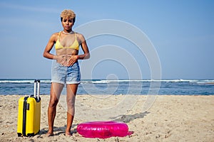 Beautiful sad and sick african american woman in yellow swimsuit and denim shorts holding hands on stomach and feeling
