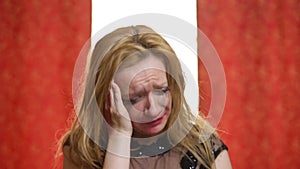 Beautiful sad woman with red lipstick and makeup cries on a red against white background. Makeup and mascara are smeared