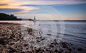 Beautiful sailboat sunset landscape with rocky silhouette beach shore