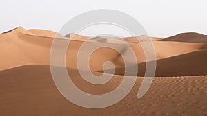 Beautiful sand dunes with wind blowing sand, backlit, in the Sahara desert, Erg Chigaga, Morocco. Serene nature backgrounds 4k foo