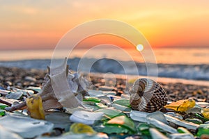 Beautiful sandy beach with sea glass, shells and pebbles sparkling under the warm sun at sunset with waves and calm sea, suitable