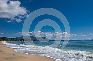 Beautiful sandy beach, sea waves, foam, blue sky, white clouds.