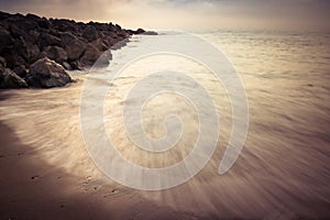 Beautiful sandy scenic beach in sunset, with rocky breakwater in long exposure in basque country, france, creative background