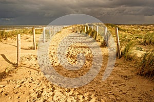 A beautiful sandy trail along the ocean. Sunshine and dark clouds in the sky. North Holland dune reserve, Egmond aan Zee,