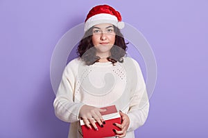 Beautiful Santa Girl with Christmas holidays gift in red box, lady looking directly at camera with serious expression, girl wears