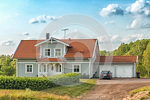 Beautiful scandinavian style house with two places garage and car in front of it. Summer with blue sky and green grass