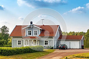 Beautiful scandinavian style house with two places garage and gar in fron of it. Summer with blue scky and green grass