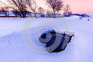 Beautiful scene with a heart shaped hole on the snow field in winter at dusk