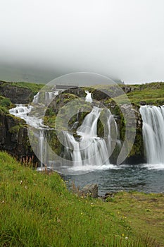 Beautiful scene of Kirkjufellsfoss waterfall with green grass on a cloudy day