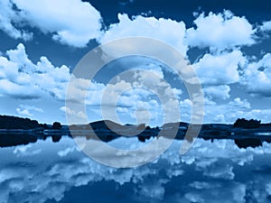 Beautiful scenery of cloudy sky, mountains and lake with reflection. Color of the year 2020 - Classic Blue