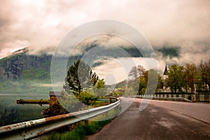 Beautiful scenery of a curved road with rustic railing on the side against a foggy mountain